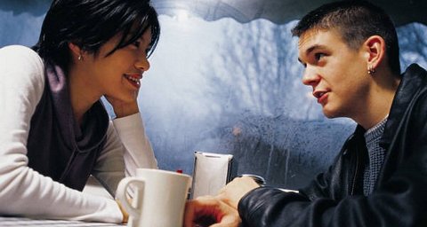 Valentine: Young man and woman gazing into each other's eyes across a table with coffee cups on it.