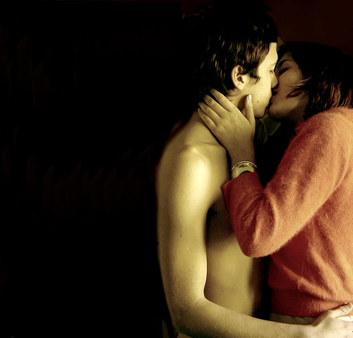 Bare-chested young man kissing fully dressed young woman.