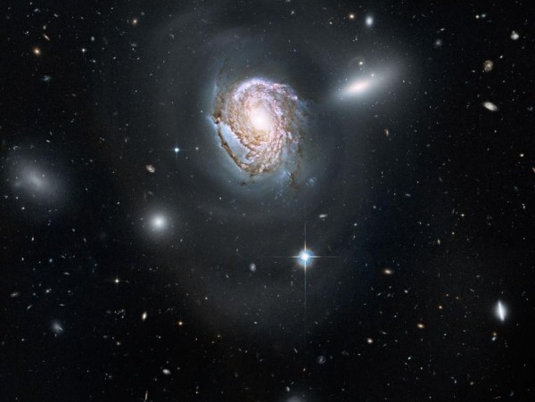 Large detailed spiral galaxy with smaller fuzzy oblong galaxies behind it.