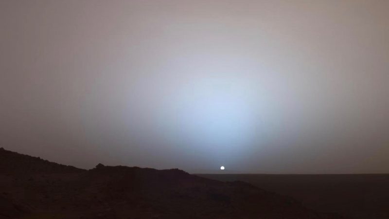 Sunset on Mars. View full of dust. Tiny sun with dark land in foreground.
