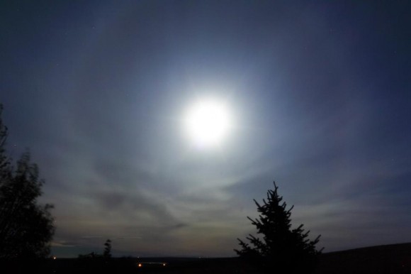 Faint halo around the bright moon among wispy clouds.