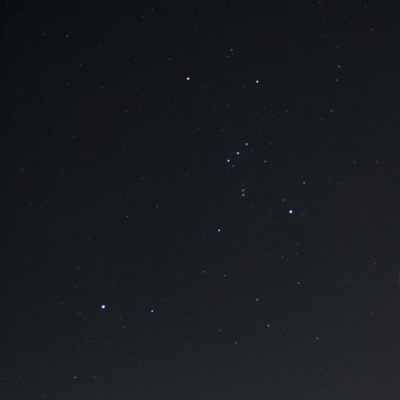 Constellation Orion standing high in sky with bright star to its lower left.