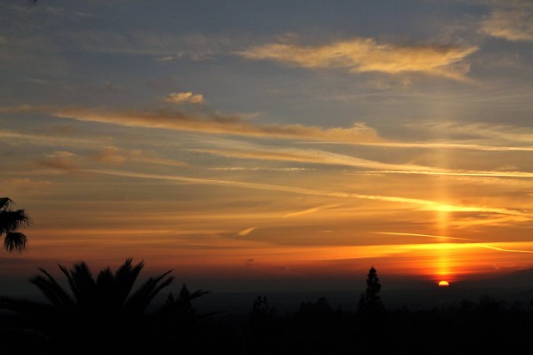 Yellow and red horizontal sunset clouds with narrow vertical light pillar from top edge of sun at horizon.