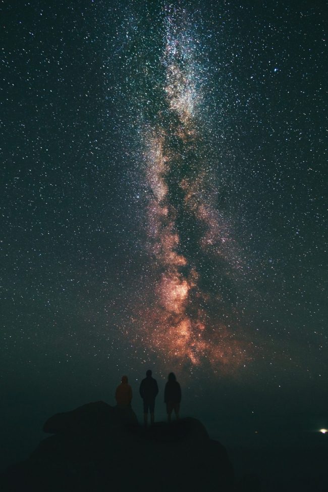 Three people stand and stare at the Milky Way.