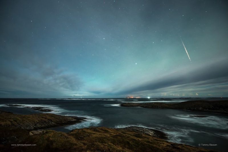 Streak of light in night sky over water and rock.