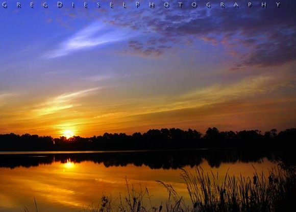 Orange-yellow sunrise under dark blue sky reflected in water.