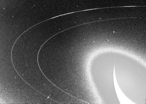 Neptune's rings: Overexposed crescent planet with two distinct thin white rings around it against black background.