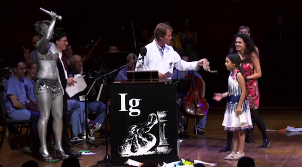 2013 Ig Nobel Archaeology Prize winner Brian Crandall presents Miss Sweetie Poo with a shrew. Looking on is a human spotlight, covered in silver body paint. Image credit: Improbable Research Inc. 