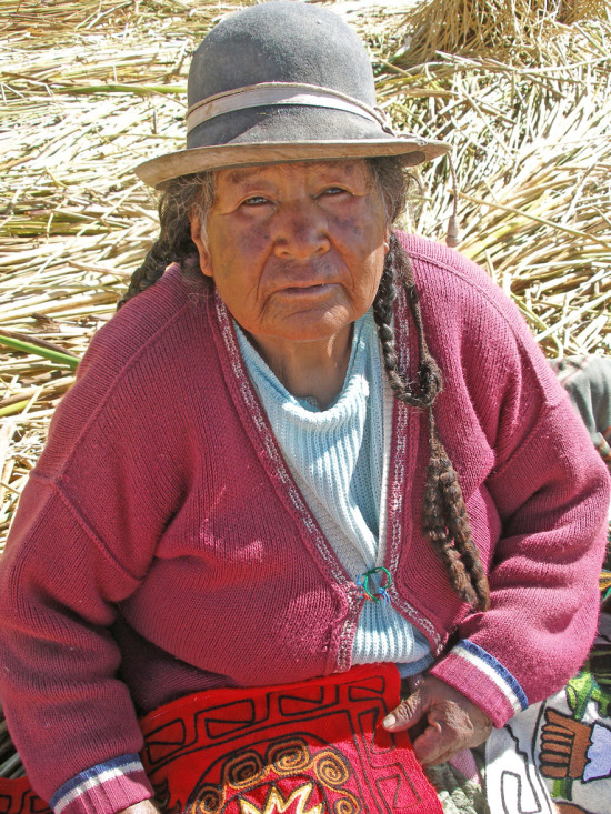 An elderly Uros woman holding embroidery, Uros Islands, Lake Titicaca, Peru, April 2012. Image via Quinet and Wikimedia Commons.