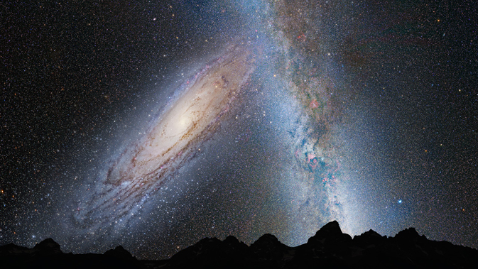 Huge oblique galaxy looming over a dark horizon with the Milky Way to one side.