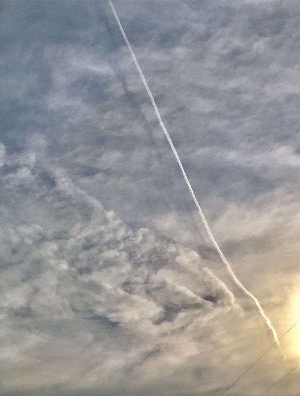 Impressionistic style clouds with a diagonal white jet contrail and its shadow.