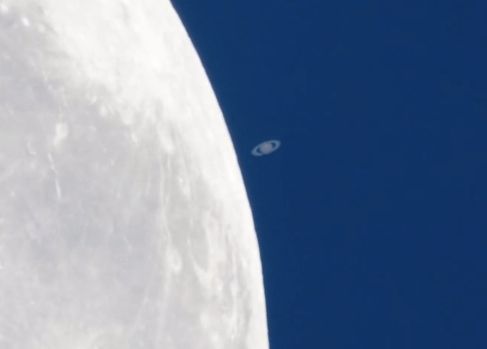 White curve of moon's surface with tiny ringed planet next to it.