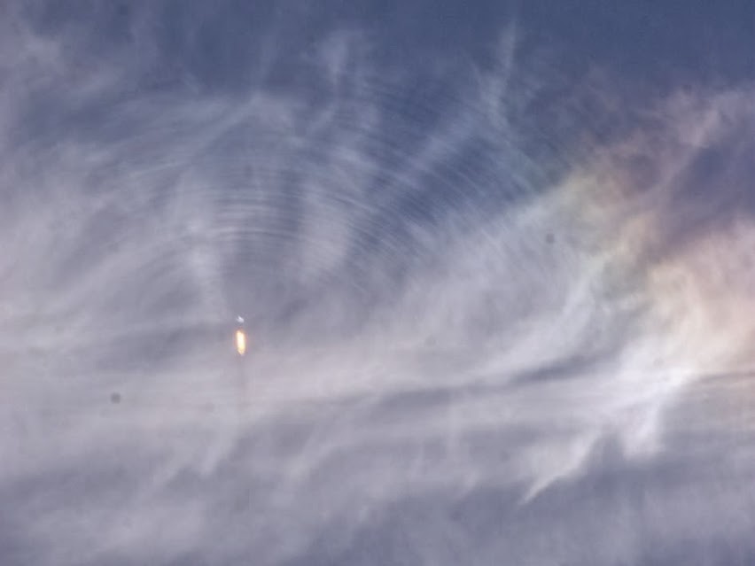 Výfuk vzdálené zářící rakety je obklopen jemnými kruhovými čarami v oblacích.