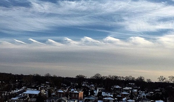 Elongated wave clouds below horizontal clouds and above snowy landscape.