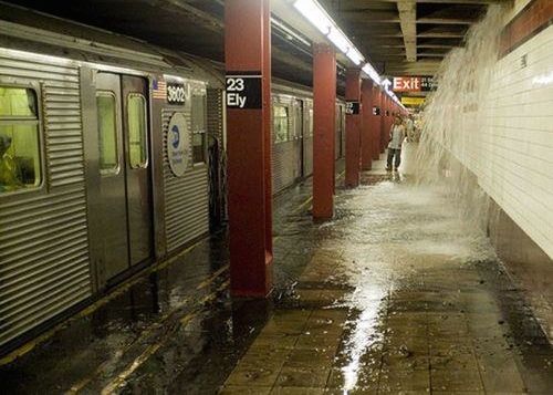 A man waits for the subway while a big amount of water falls like a waterfall from the roof.
