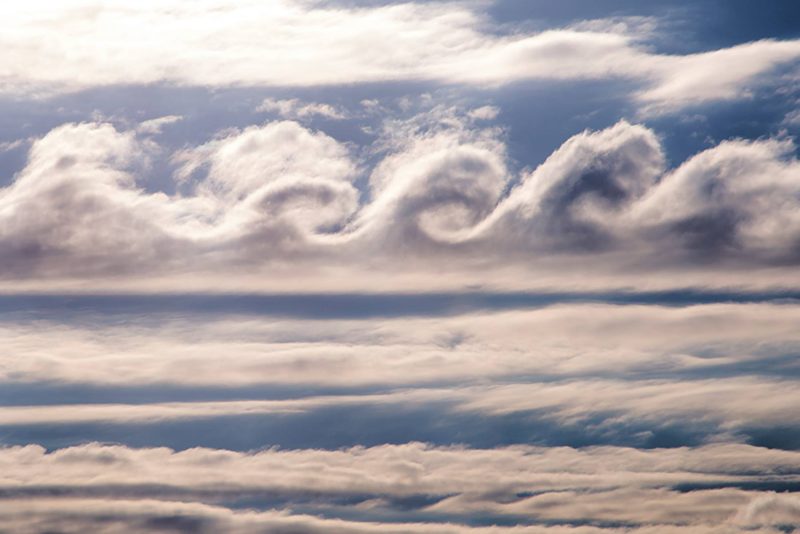 Very round vertical eddies in cloud stripe in sky with other horizontal clouds.
