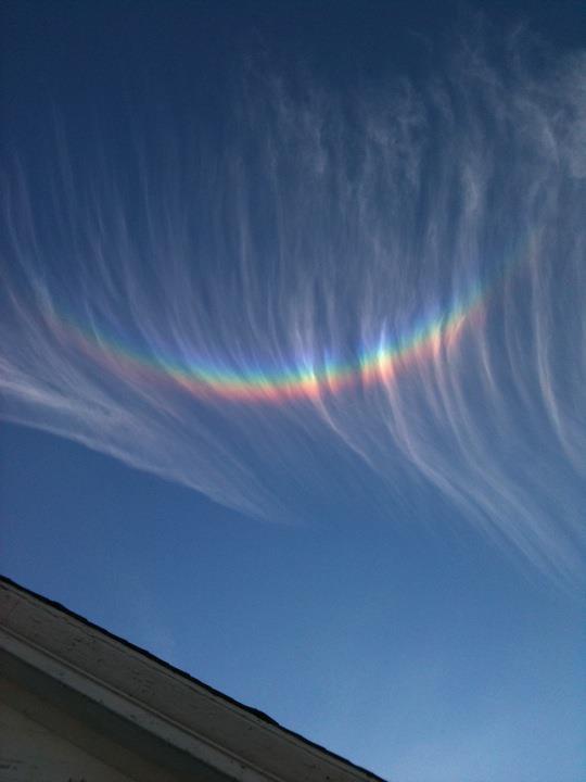 Long parallel streamer-like clouds in a blue sky with very bright arc across them.