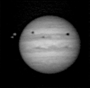 Three dark spots on slightly fuzzy telescopic view of Jupiter.