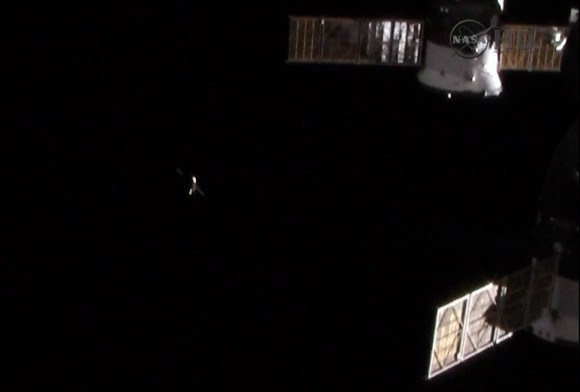 View larger. | The ISS Progress 53 cargo ship can be seen in the distance following its undocking from the International Space Station. Another Progress and a Soyuz spacecraft, both docked to the station, can be seen on the right. Image credit: NASA TV