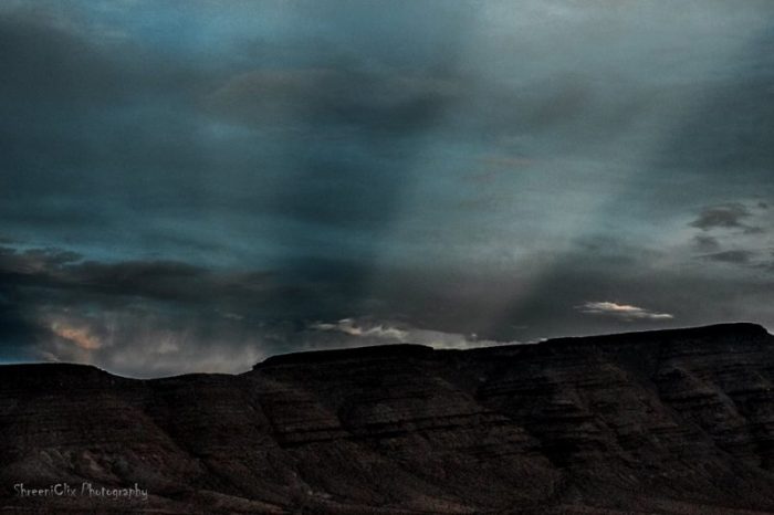 Wide light rays through clouds over a mountain landscape.