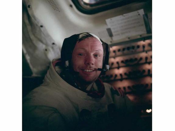 Boyish looking man in space suit with helmet off grinning at the camera.