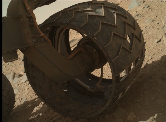 View larger. | A puncture (center right) in one of the Mars rover Curiosity’s wheels. (The sequence of cutouts at lower right are deliberate and imprint ‘JPL’ in Morse code as the wheels roll across the Martian surface.)  Image via NASA/JPL-CALTECH/MSSS, Nature.