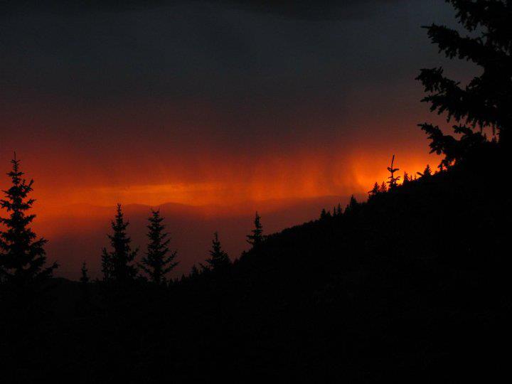 Dark virga against a strip of deep orange sky between layers of dark clouds.