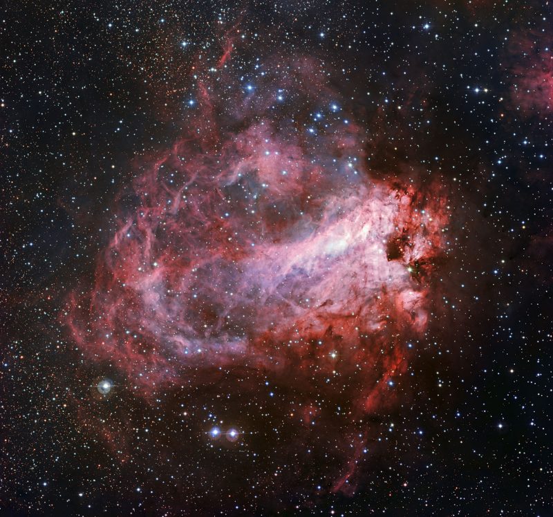 Large pink glob made of many wisps of gas in dense star field.