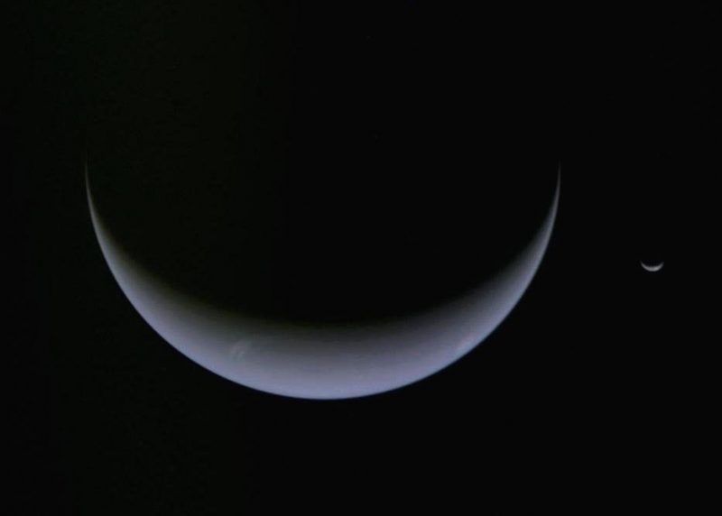 A large blue crescent Neptune, next to a tiny blue crescent Triton.