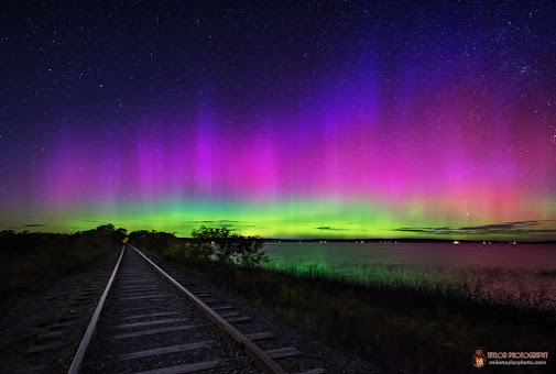 Green, pink and blue glow over train tracks.