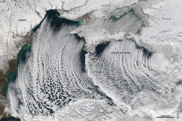 Many curved parallel lines of clouds seen from orbit in black and white.