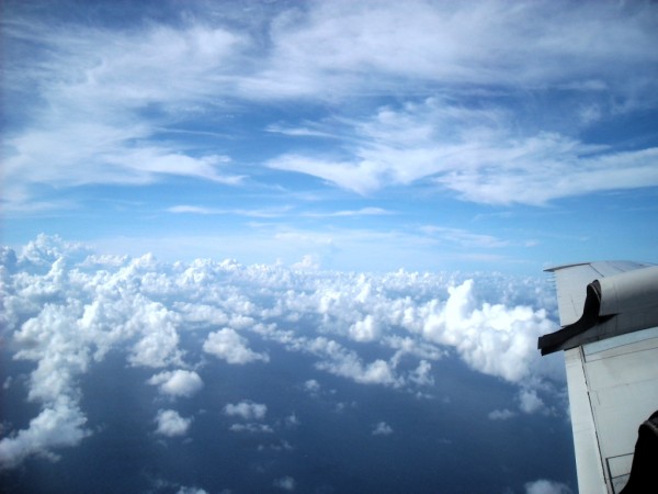 Rows of puffy cumulus clouds seen from above with part of airplane wing visible.