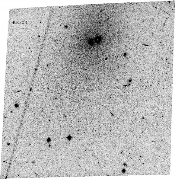 A negative image of KKs 3, made using the Advanced Camera for Surveys on the Hubble Space Telescope. The core of the galaxy is the right hand dark object at the top centre of the image, with its stars spreading out over a large section around it. (The left hand of the two dark objects is a much nearer globular star cluster.)  Image credit: D. Makarov. 