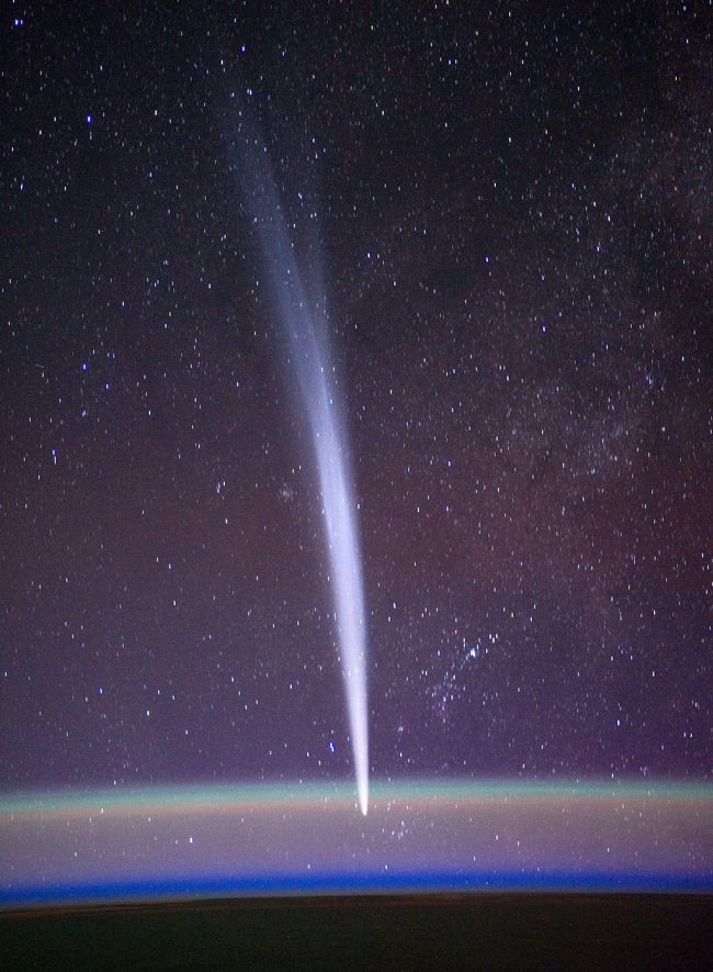 A beautiful comet with a long tail seen over hazy curve of Earth.