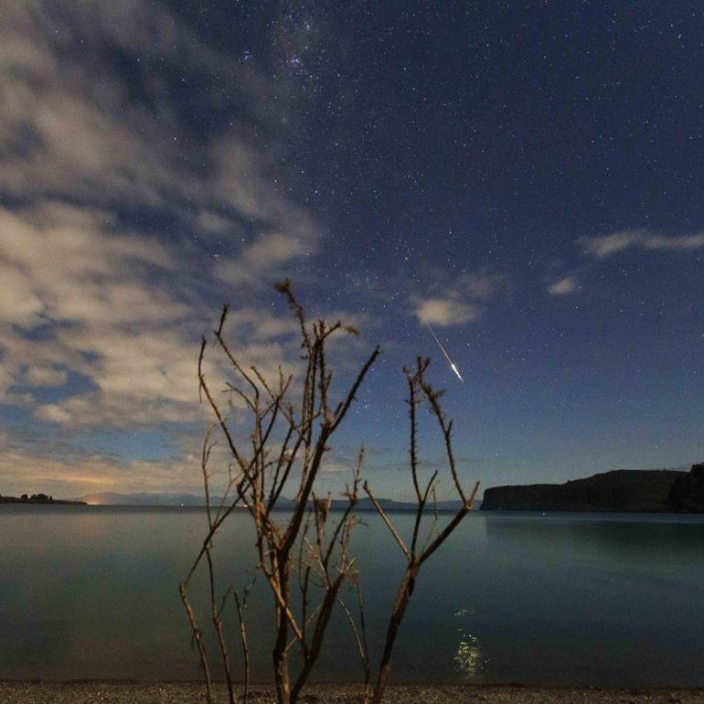 Meteor and partly cloudy sky over lake and bare branches, above Taupo supervolcano.