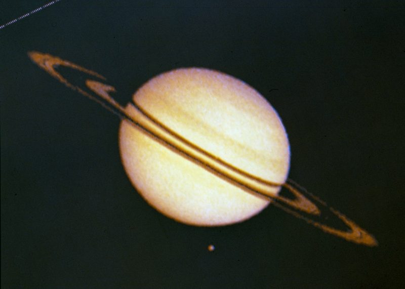 Pioneer 11: Golden ball of Saturn, surrounded by nearly edgewise rings, and a little dot of a moon.