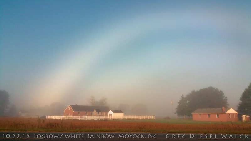 Partial white arc over bucolic scene with white fence and barn in distance.