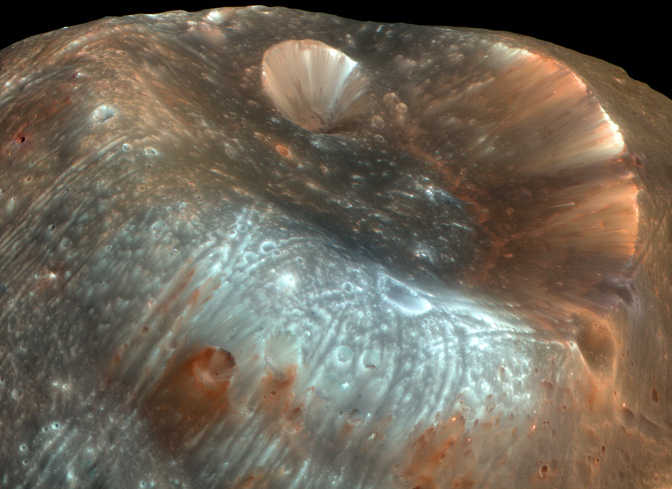 Very large crater on blue and pink landscape with many small craters.