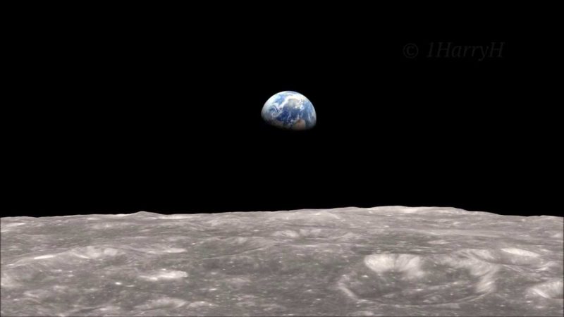 Distant half Earth floating in black sky over gray, cratered surface of the moon.