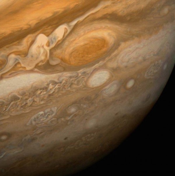 View of a small part of Jupiter showing orangish and brown colors and the Great Red Spot with white whorls nearby.