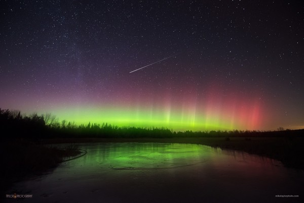 The green glow of northern lights on the horizon with a bright meteor streaking above.