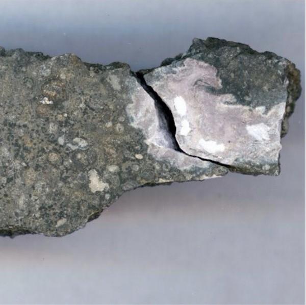 A close-up photo of a meteorite sample, 0.59 inches (1.5 centimeters) across showing a ceramic-like refractory inclusion (in pink) embedded in the meteorite. Refractory inclusions are the oldest-known rocks in the solar system (4.5 billion years old). The analysis of the uranium isotope ratios of such inclusions showed that a long-lived curium isotope was present early in the solar system when this inclusion was formed.  Image credit: Origins Lab, University of Chicago.