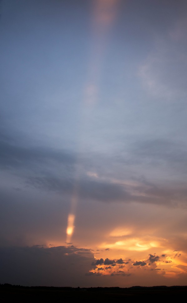 Pillar of light coming up from dark clouds against a yellow sunset.