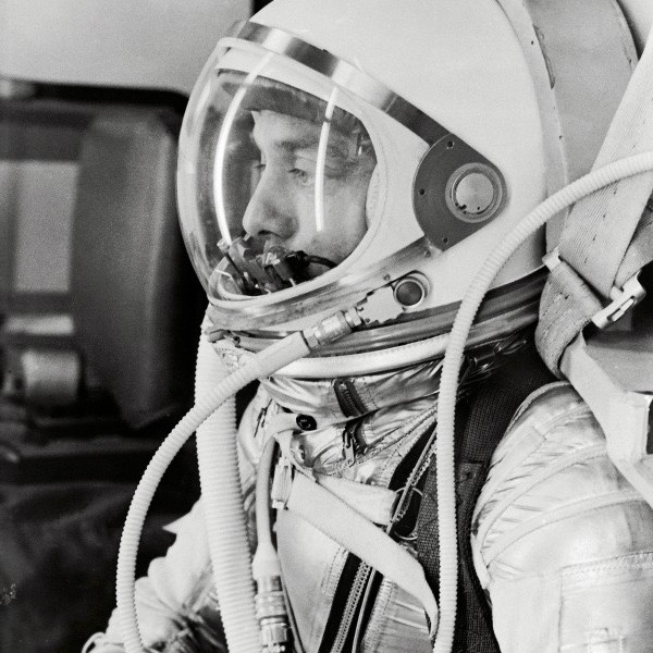 American in space: Young man's face seen through clear helmet visor, plastic pipes running from helmet to space suit.