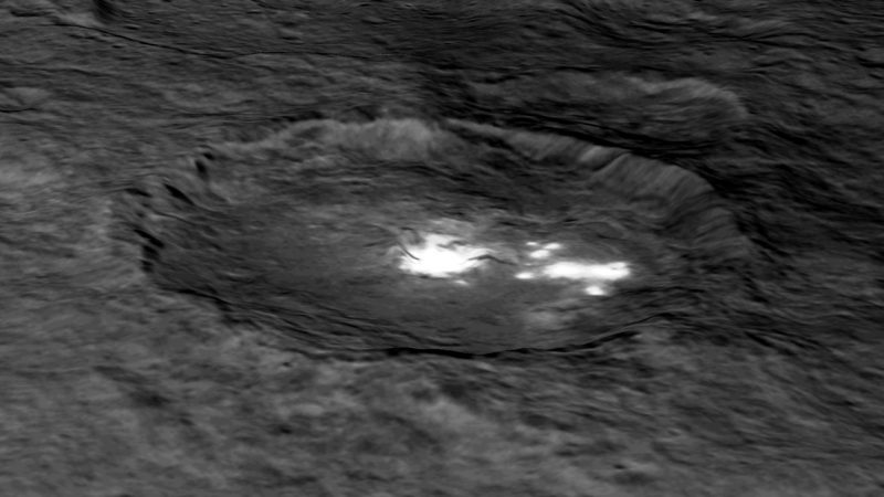 Oblique view of a crater on irregular terrain with very bright white patchs.