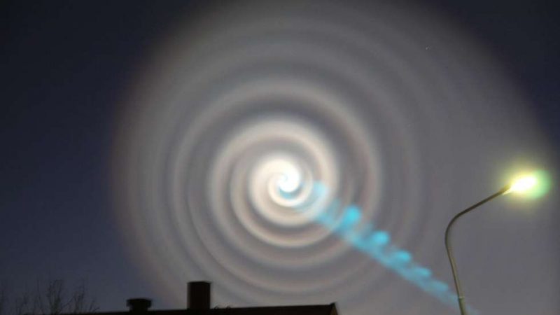 Concentric circles in the night sky with a blue gaseous corkscrew spiral coming out of the center.