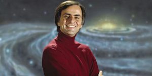 Carl Sagan: Smiling man in red turtleneck shirt against a mural painting of a galaxy.