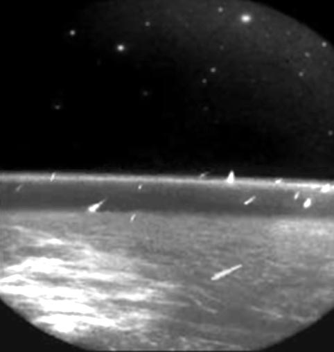 12 small objects streaking toward Earth as seen from orbit in black and white.