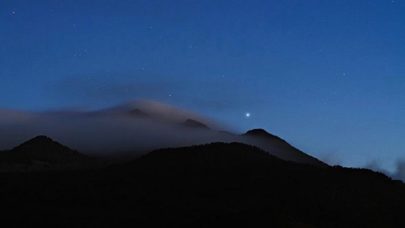 A single bright star in a deep blue sky above a foggy mountain.