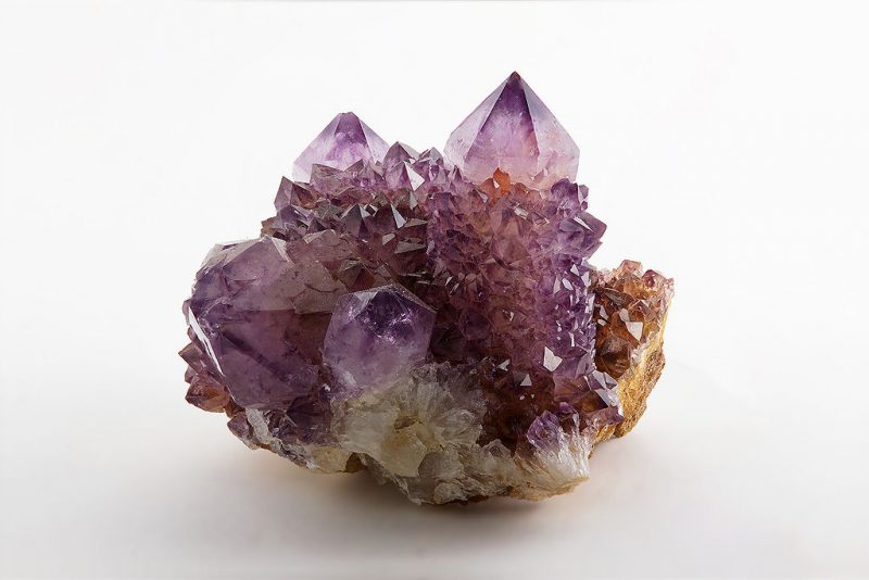 Large, pointed purple crytals growing from a rock with tiny crystals between them.